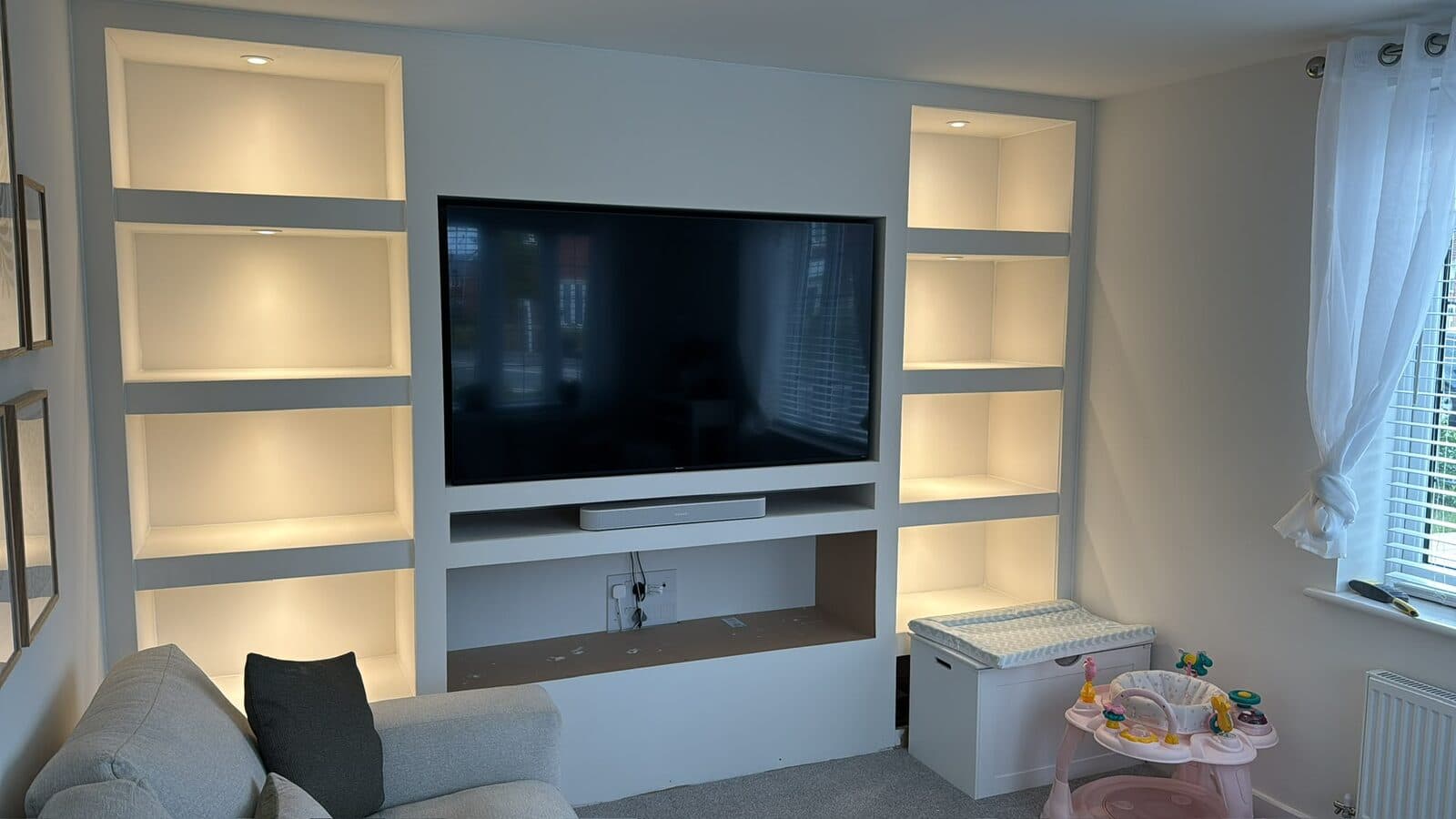 Media wall in a living room with warm LED lighting in the shelves either side of the TV